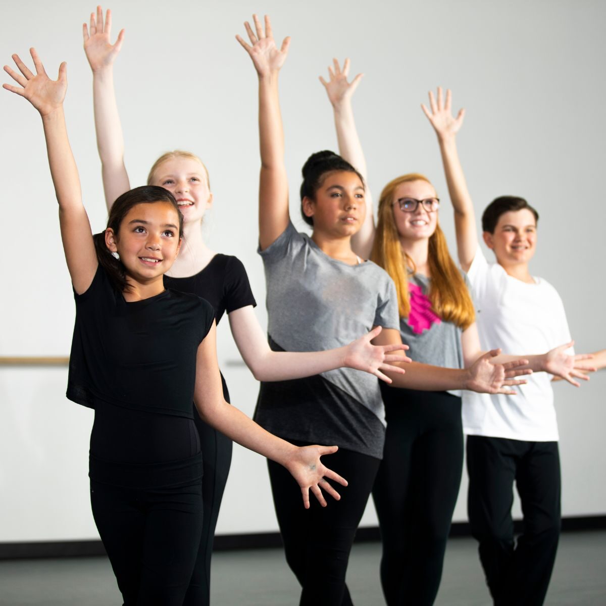 A diverse group of five individuals stands in a line with raised arms, wearing casual dance attire in a studio setting—an inspiring moment reflecting their journey through adult education classes.